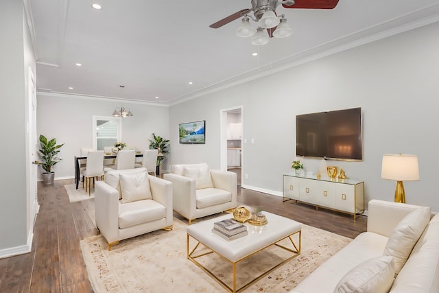 living room with wood-type flooring, ceiling fan with notable chandelier, and ornamental molding