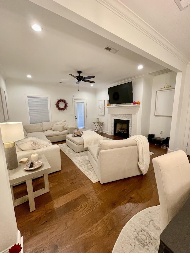 living room with dark hardwood / wood-style floors, ceiling fan, a premium fireplace, and crown molding