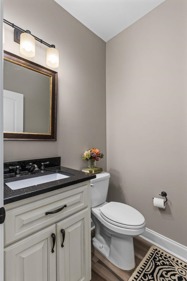 half bath with vanity, baseboards, toilet, and wood finished floors