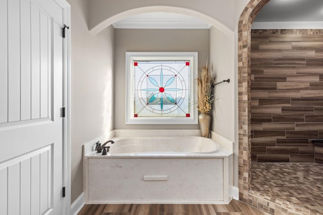bathroom featuring ornamental molding, wood finished floors, baseboards, a bath, and a tile shower