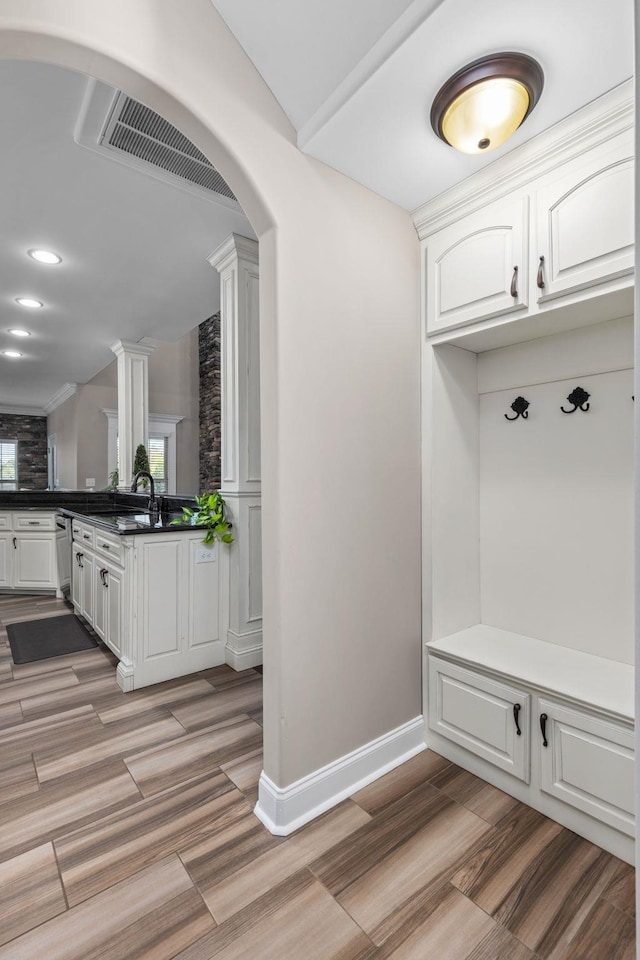 mudroom with decorative columns, visible vents, arched walkways, light wood-type flooring, and baseboards