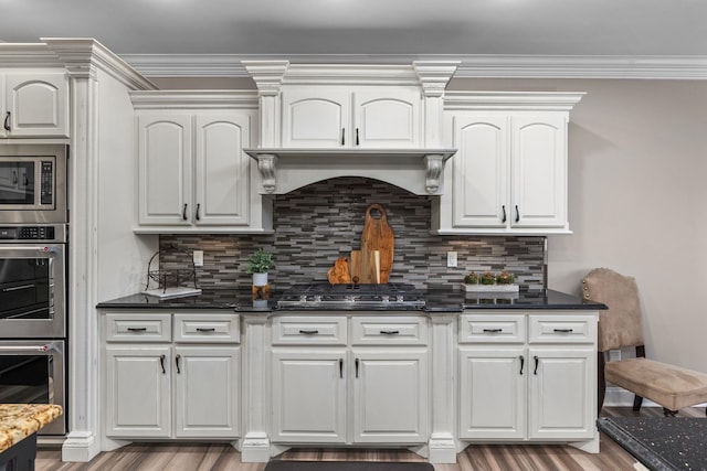 kitchen featuring backsplash, appliances with stainless steel finishes, wood finished floors, dark stone countertops, and white cabinetry