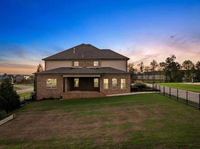 back of house at dusk with brick siding, a fenced backyard, and a yard