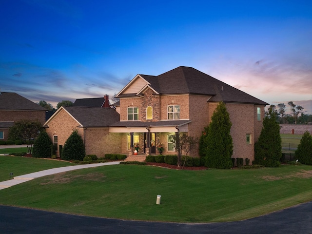 traditional home with brick siding, a yard, and covered porch