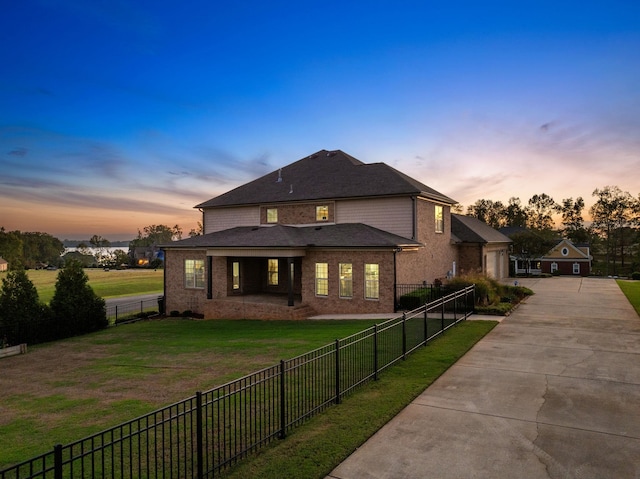 back of property featuring a fenced backyard, concrete driveway, a yard, and brick siding