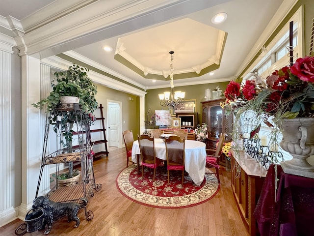 dining room featuring ornate columns, a raised ceiling, crown molding, wood-type flooring, and an inviting chandelier