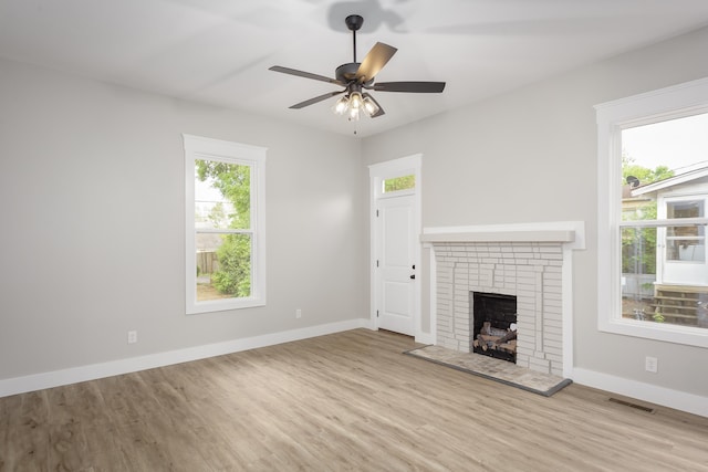 unfurnished living room with a ceiling fan, visible vents, a brick fireplace, wood finished floors, and baseboards