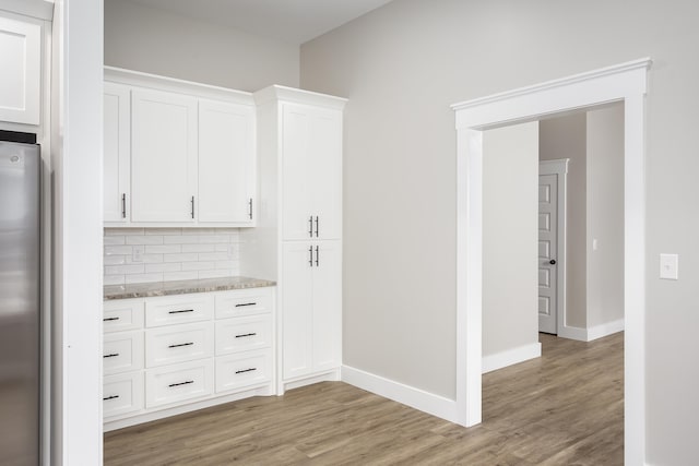 kitchen with freestanding refrigerator, light wood-type flooring, white cabinets, tasteful backsplash, and light stone counters