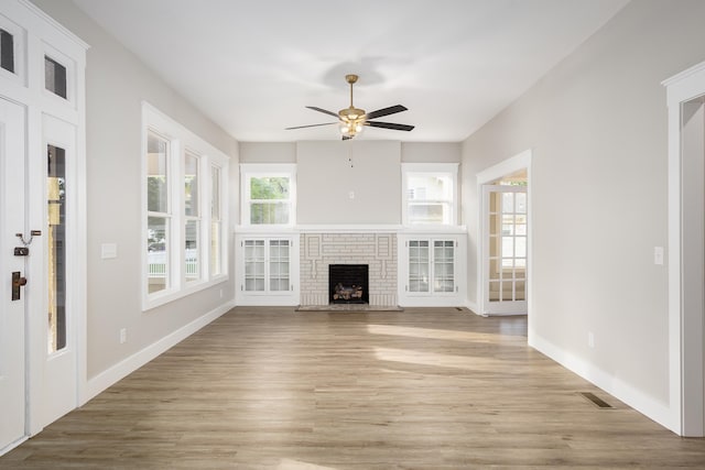 unfurnished living room with a ceiling fan, visible vents, a brick fireplace, light wood-type flooring, and baseboards