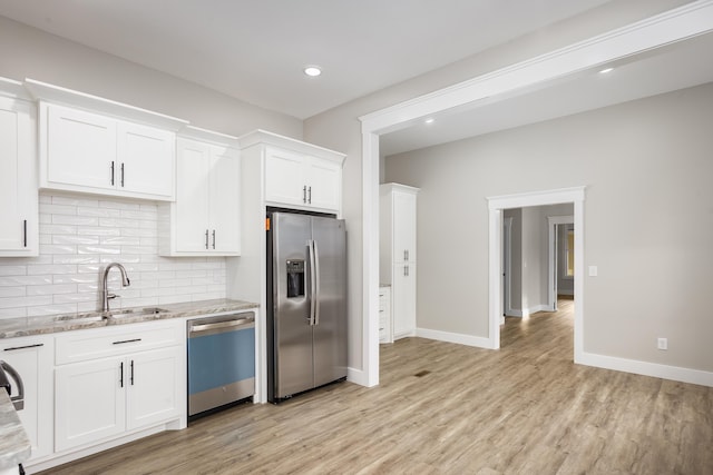 kitchen with light stone countertops, a sink, stainless steel appliances, white cabinetry, and decorative backsplash