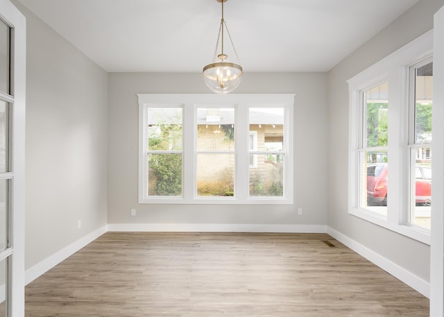 unfurnished dining area featuring baseboards, light wood finished floors, and a notable chandelier