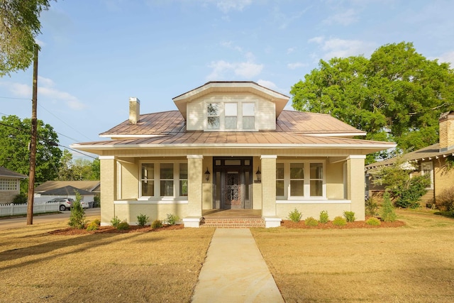 bungalow-style home with covered porch, a standing seam roof, metal roof, a front yard, and brick siding