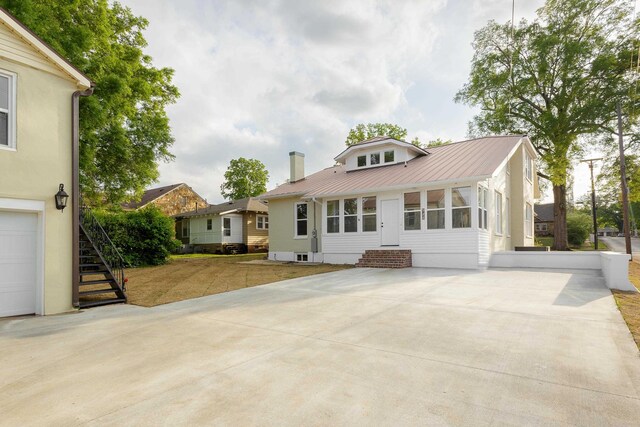 back of house with metal roof, a chimney, entry steps, driveway, and stairway