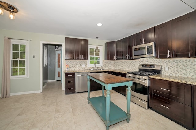  - kitchen with stainless steel appliances, decorative backsplash, dark brown cabinetry, baseboards, and decorative light fixtures