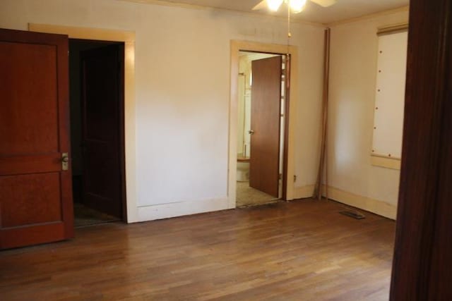 unfurnished bedroom featuring ceiling fan, wood-type flooring, crown molding, and ensuite bath