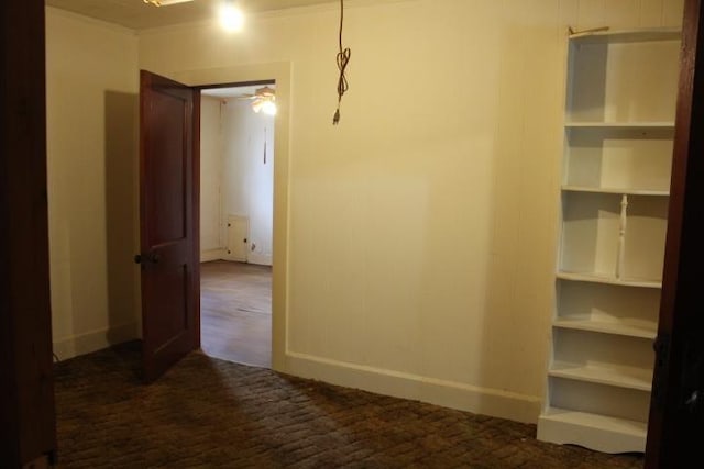 corridor with built in features, ornamental molding, and dark colored carpet