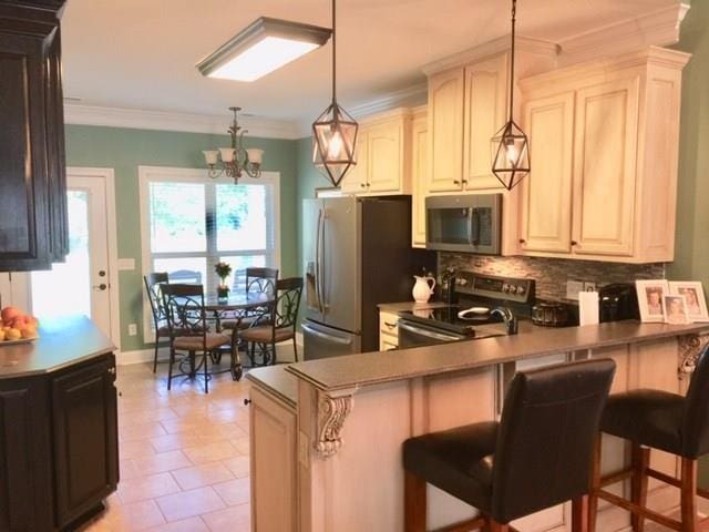  - kitchen with appliances with stainless steel finishes, backsplash, a chandelier, a peninsula, and decorative light fixtures