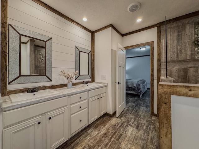 bathroom with wood walls, a textured ceiling, ornamental molding, vanity, and hardwood / wood-style floors