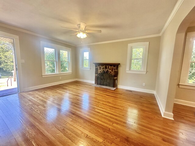 unfurnished living room with ceiling fan, light hardwood / wood-style floors, a stone fireplace, and crown molding