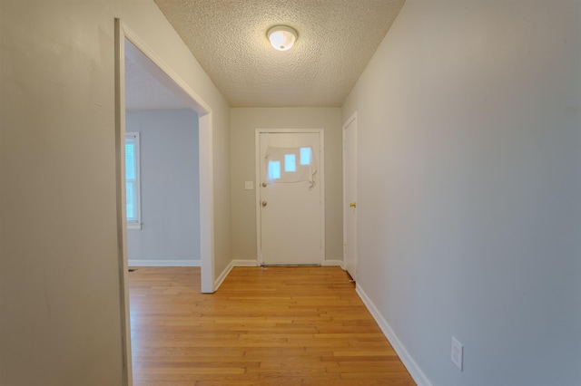 doorway to outside with light wood-style flooring, baseboards, and a textured ceiling