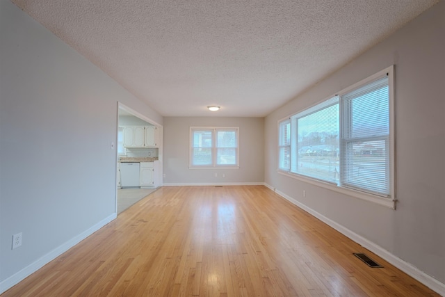 unfurnished living room featuring a textured ceiling, light wood-type flooring, visible vents, and baseboards