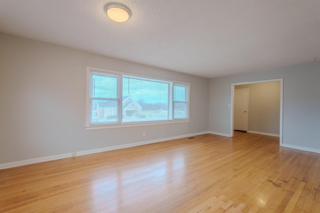 empty room with light wood-style floors, visible vents, a textured ceiling, and baseboards