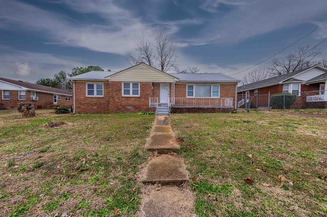 view of front of property with brick siding, a front yard, crawl space, fence, and metal roof