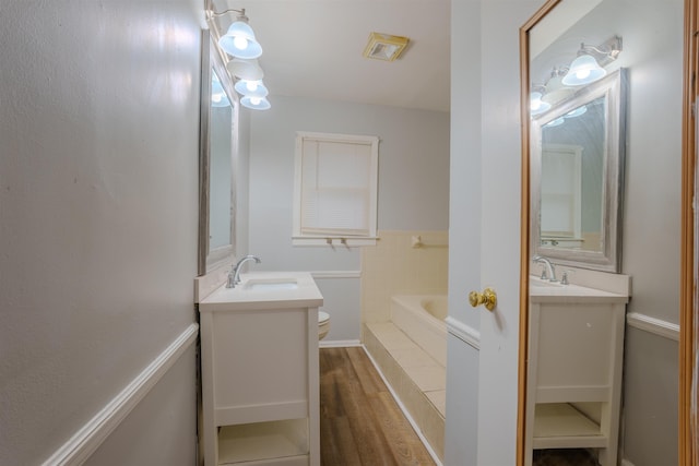 bathroom featuring toilet, two vanities, a sink, and wood finished floors