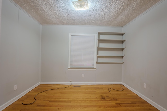 empty room with baseboards, visible vents, wood finished floors, crown molding, and a textured ceiling