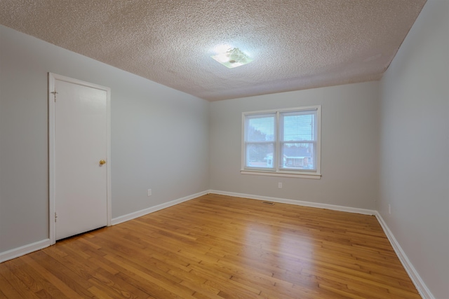 spare room featuring light wood-style floors, baseboards, and a textured ceiling