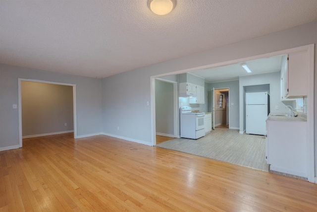 unfurnished living room featuring light wood-type flooring, a sink, and baseboards