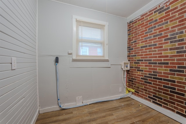 laundry area featuring brick wall, ornamental molding, and wood finished floors