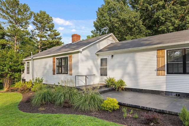  - view of side of home with a patio area, a chimney, and roof with shingles