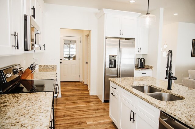 kitchen featuring appliances with stainless steel finishes, light stone counters, sink, white cabinetry, and hanging light fixtures