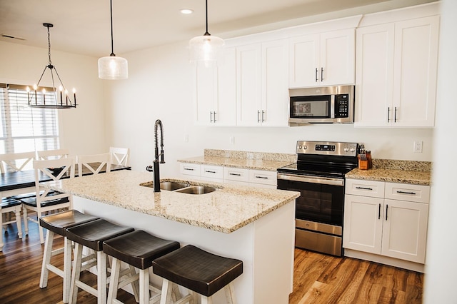 kitchen with appliances with stainless steel finishes, a kitchen island with sink, sink, decorative light fixtures, and white cabinets