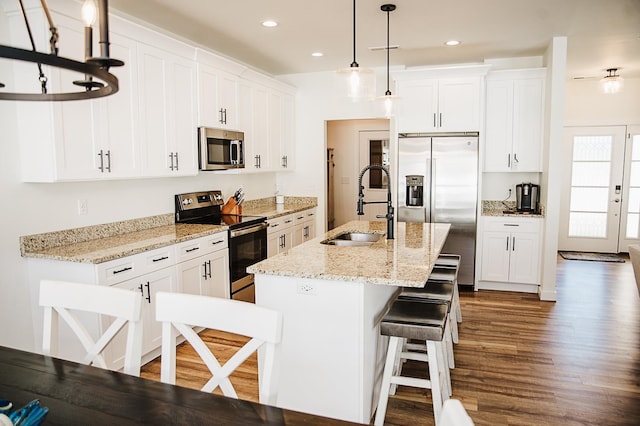 kitchen featuring stainless steel appliances, sink, pendant lighting, white cabinetry, and an island with sink