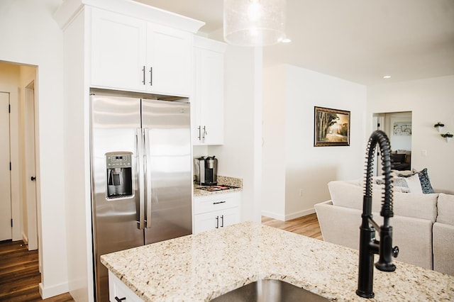 kitchen with light stone counters, wood-type flooring, white cabinets, stainless steel fridge with ice dispenser, and hanging light fixtures