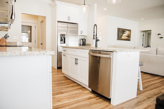 kitchen featuring white cabinets, decorative light fixtures, appliances with stainless steel finishes, and light hardwood / wood-style flooring