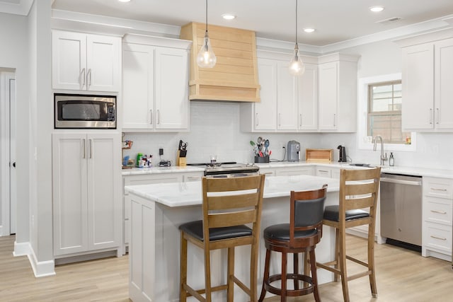 kitchen with a center island, white cabinets, sink, appliances with stainless steel finishes, and decorative light fixtures