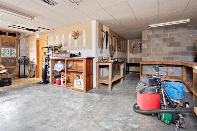 interior space featuring a workshop area, a drop ceiling, visible vents, and concrete block wall