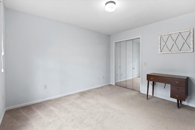 bedroom featuring a closet, light carpet, a textured ceiling, and baseboards