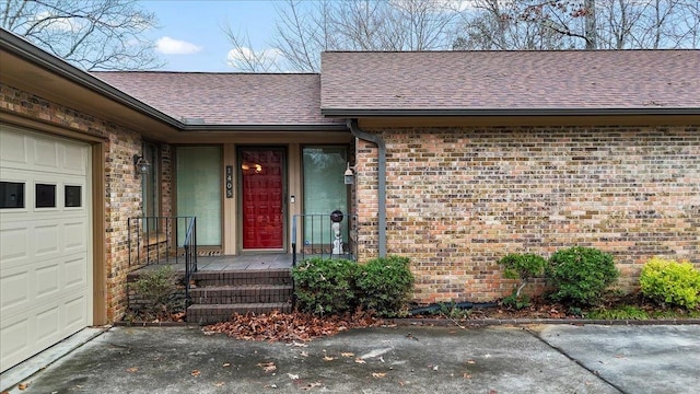 entrance to property featuring a garage, brick siding, and roof with shingles