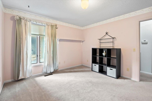 empty room featuring a textured ceiling, carpet, visible vents, and baseboards