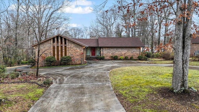 mid-century modern home featuring a front yard, brick siding, curved driveway, and a chimney