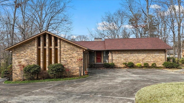 mid-century modern home with brick siding, driveway, and a chimney