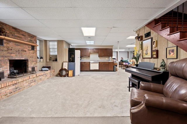 living area featuring a brick fireplace, light colored carpet, stairway, and a drop ceiling