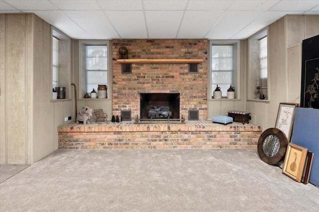 carpeted living room with a paneled ceiling, a brick fireplace, and visible vents