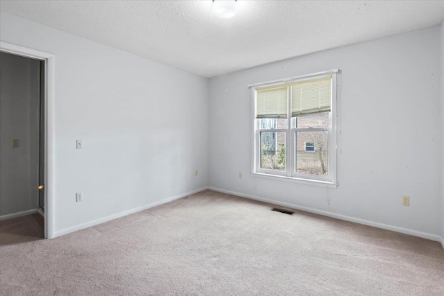 carpeted spare room with a textured ceiling, visible vents, and baseboards