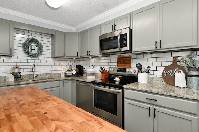 kitchen featuring wooden counters, appliances with stainless steel finishes, tasteful backsplash, a textured ceiling, and sink