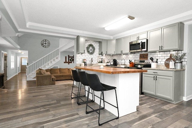 kitchen with wood counters, dark hardwood / wood-style floors, gray cabinets, a kitchen bar, and stainless steel appliances